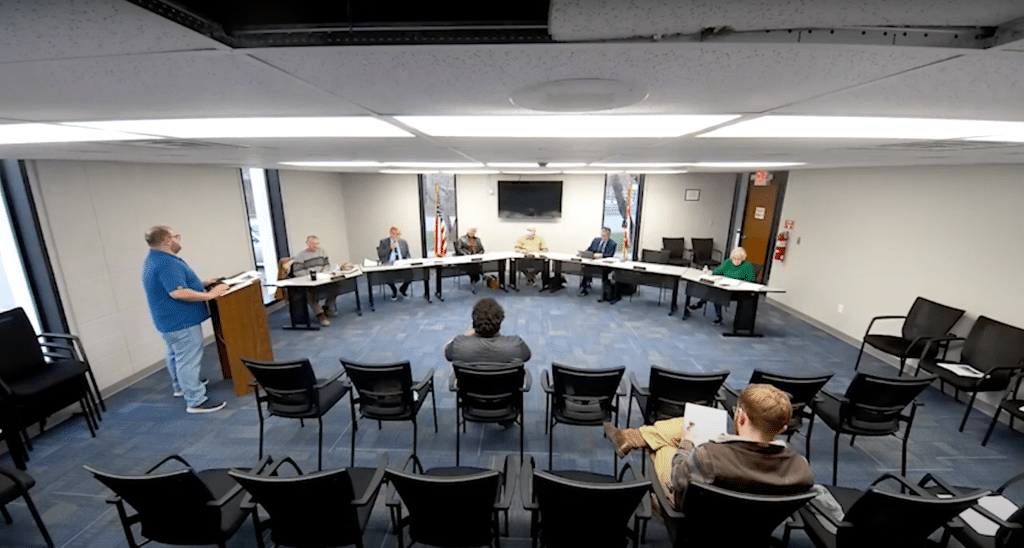 A man stands at a podium before city council and the public.